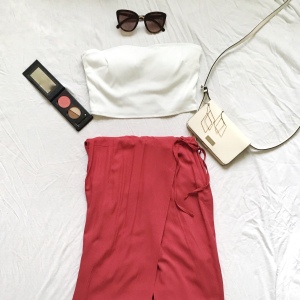 White swimsuit tube top with a red skirt and a white purse with other accessories around the outfit